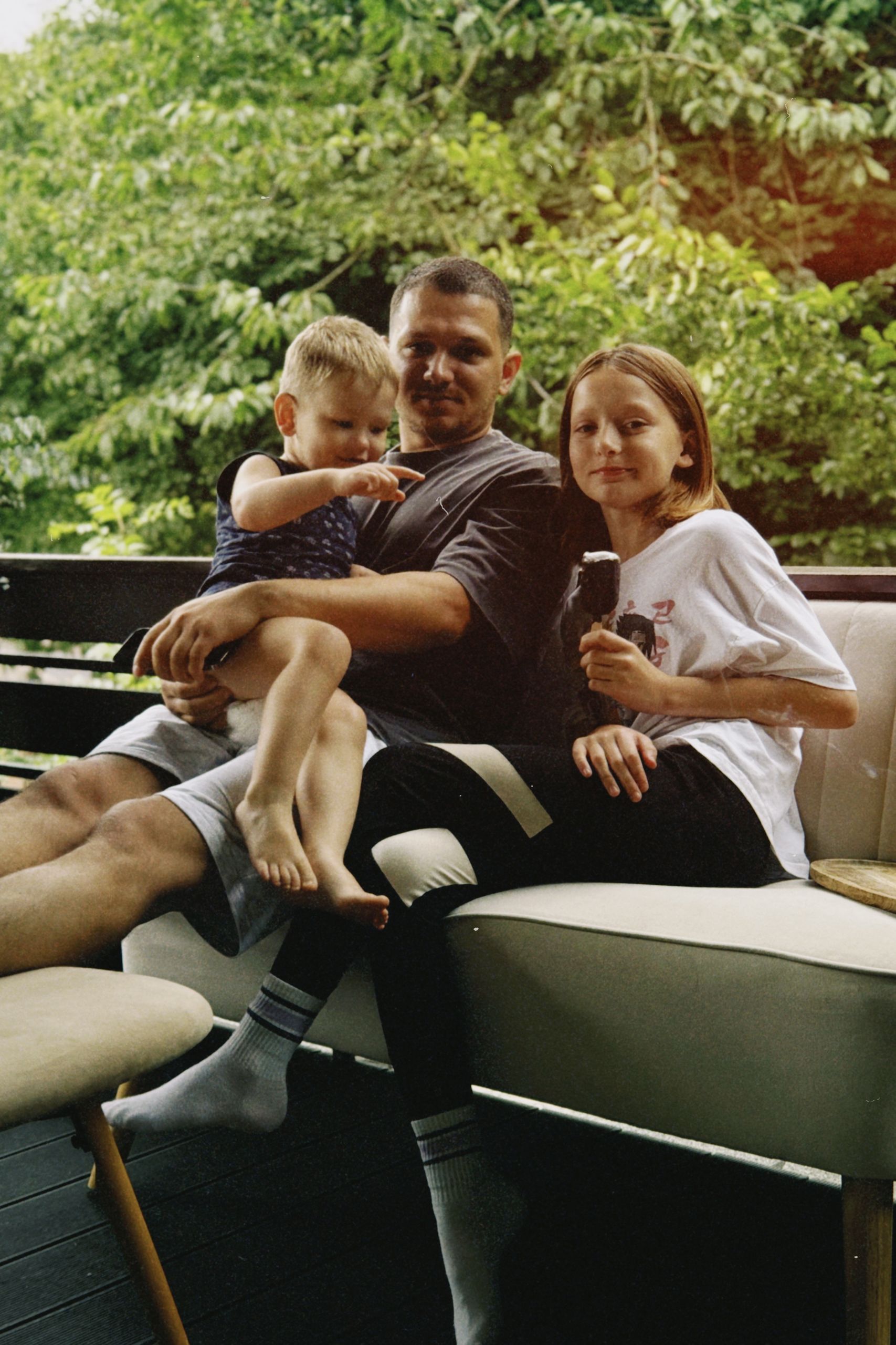 A father with his two children enjoying time together on a cozy outdoor sofa.
